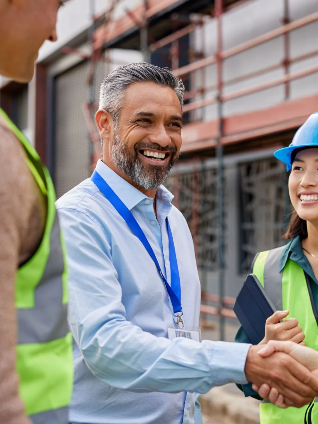 Rakennustyömaan johto ja työntekijät kättelevät ja keskustelevat hymyillen, taustalla rakennustelineet.